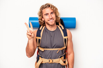 Wall Mural - Young mountaineer caucasian man with a big backpack isolated on white background joyful and carefree showing a peace symbol with fingers.