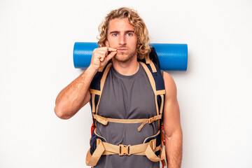 Wall Mural - Young mountaineer caucasian man with a big backpack isolated on white background with fingers on lips keeping a secret.