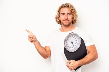 Wall Mural - Young woman holding a scale isolated on white background smiling and pointing aside, showing something at blank space.