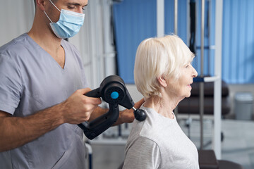 Wall Mural - Physiotherapist treating pensioner shoulder with muscle massage gun