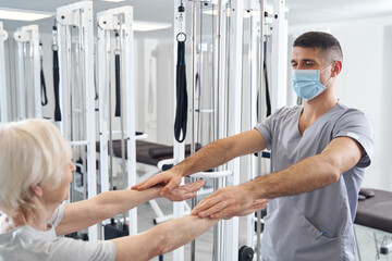 Wall Mural - Physiotherapist holding his hands above arms of aged woman