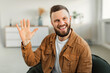 © Prostock-studio - Joyful Man Waving Hand Smiling To Camera Sitting At Home