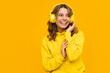 © mary_markevich - smiling attractive woman listening to music in headphones on yellow background