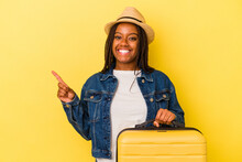 Young African American Traveler Woman Holding Suitcase Isolated On Yellow Background  Smiling And Pointing Aside, Showing Something At Blank Space.