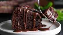 Chocolate Fudge Cake With Chocolate Glaze Sauce On A Plate, Taking Bite With A Fork. Closeup View