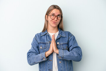 Young caucasian woman isolated on blue background holding hands in pray near mouth, feels confident.