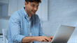 smiling freelancer in blue shirt typing on laptop in kitchen