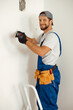 © Kostiantyn - Happy handyman electrician smiling at camera, holding pliers while working on wiring in new house
