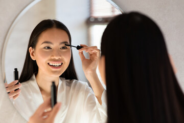 Wall Mural - Cheerful pretty japanese woman in bathrobe using mascara