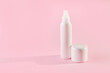 Two white plastic jars with cosmetics on a pink background with copy space