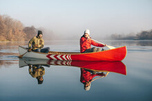 Two Men Paddling In A Wooden Canoe On A Lake With Still Water