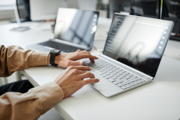 hands of young contemporary program developer typing on laptop keyboard while sitting by desk in off