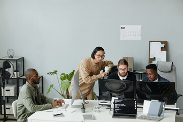 group of young contemporary program developers gathered in front of computer monitors for discussion
