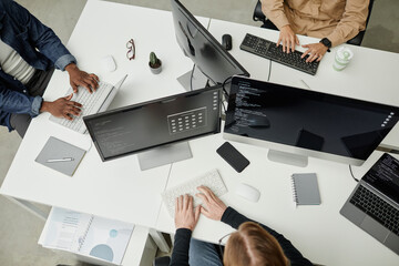 hands of young intercultural software developers typing on computer keyboards while sitting by desks