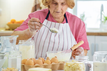 Grandmother old woman in the kitchen bakes prepares the dough in the kitchen. Selective focus.