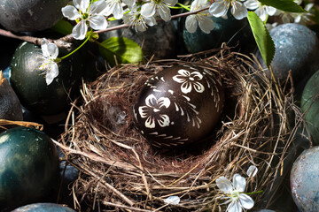 Wall Mural - Decorated in white brown color traditional Easter egg in original bird nest, naturally colored eggs around with blooming in white flowers cherry branches on background, Easter holiday table decoration