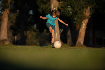 Wall Mural - Soccer kids, child boy play football outdoor. Young boy with soccer ball doing kick. Football soccer players in motion. Cute boy in sport action. Child soccer player in park.