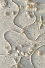 Sand background with seashells, starfish, cord and pebbles. Off white stones on textured sand surface. Summertime monochromatic flat lay. Summer beach decorations, decorative top view.