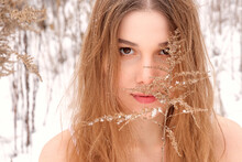 Hardened Girl Undressed In The Cold Among The Snow In The Winter Outdoors. The Girl's Face Is Close-up Behind A Branch. Winter Portrait Of A Girl.