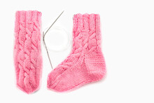Pink Knitted Socks With Aran Pattern And Knitting Needles On A White Background. Place For Text. Warm Handmade Knitted Socks With Beautiful Patterns. Traditional Crafts For Psychological Rehabilitatio