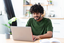 Smiling Young Indian Man Using Laptop To Work Remotely From Home, Portrait Of Successful Freelancer Or Student Working On New Project
