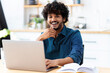 © kucherav - Portrait of a successful young Indian male freelance using laptop and looks at the camera, remote work from home, online education