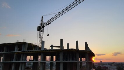 Wall Mural - Tower lifting crane and high residential apartment building with monolithic frame under construction at sunset. Real estate development