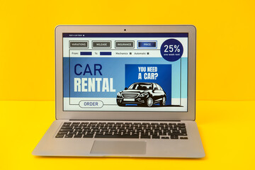 Wall Mural - Laptop with open page of car rental site on yellow background