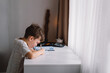 © Анастасія Стягайло - Distance learning education. Back to school. Cute kid boy studying at home and doing school homework. Thinking child sitting at table