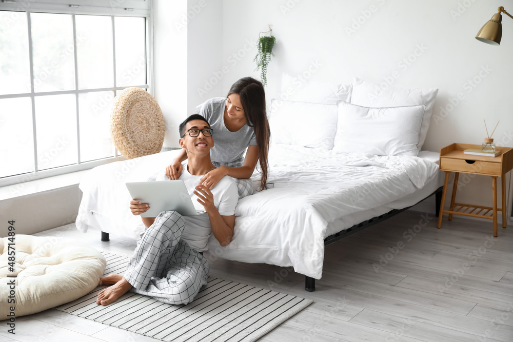 Young man with laptop and his girlfriend in bedroom
