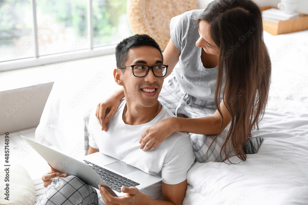 Young man with laptop and his girlfriend in bedroom