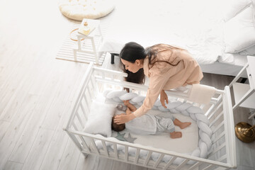 Young mother and her adorable baby sleeping in crib at home