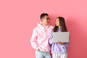 Wall Mural - Young couple with laptop on pink background
