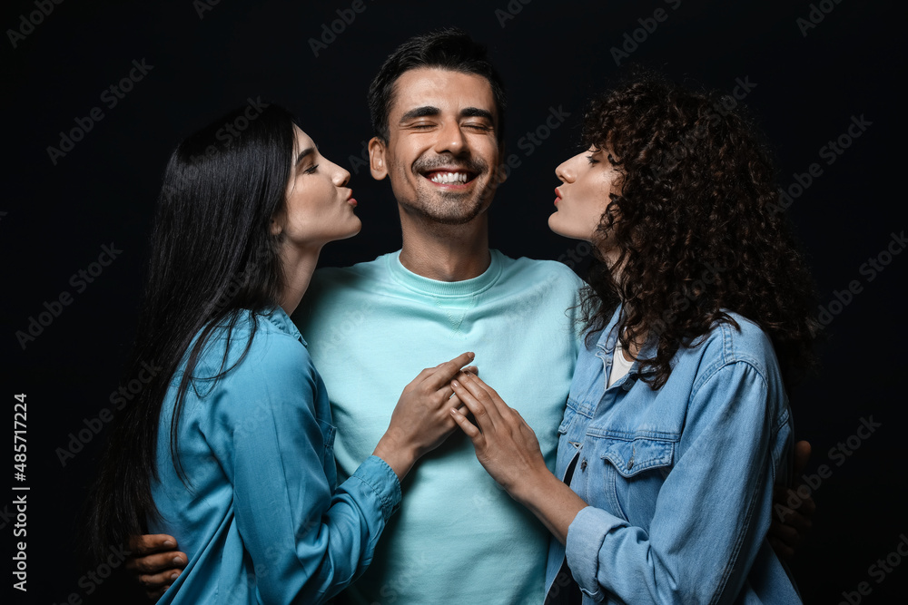 Man and two beautiful women on dark background. Polyamory concept
