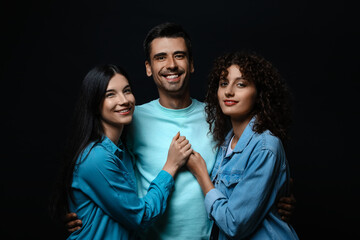 Wall Mural - Man and two beautiful women on dark background. Polyamory concept