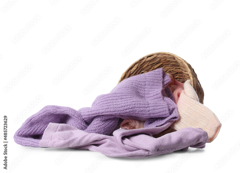 Overturned wicker basket with female sweaters on white background