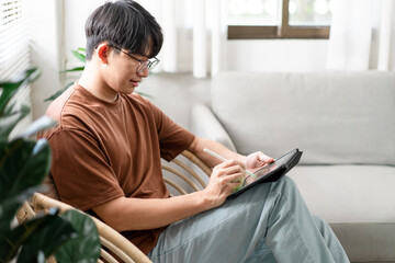 Technology Concept The young man who is sitting on the chair holding his iPad and noting something on it