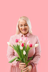 Sticker - Smiling mature woman looking at bouquet of tulips on pink background. International Women's Day celebration