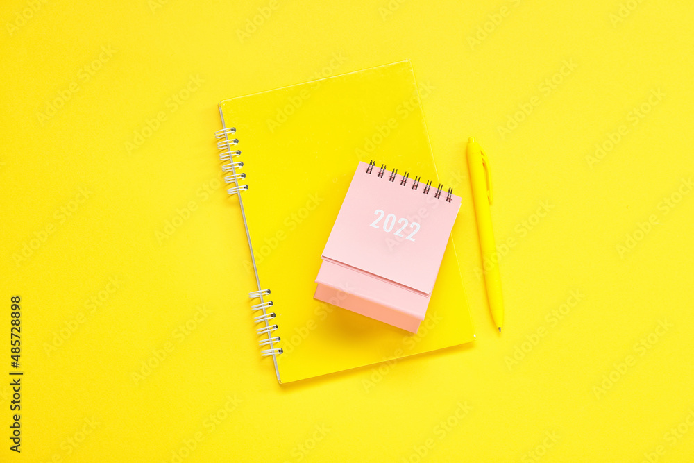 Calendar for 2022 year, notebook and pen on yellow background