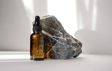 Wall Mural - Mock-up of bottle with dropper lid, made of brown glass, against background of natural stone made of gray marble. Rays of sunlight fall on white background and leave glare on objects.