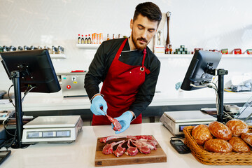 Poster - Young butcher holding raw lamb ribs in a butcher shop