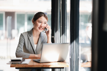 portrait of young asian business woman talk on smartphone write notebook laptop in home office. beau