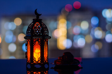 Wall Mural - Selective focus of lantern and small plate of dates fruit with apartment building background for the Muslim feast of the holy month of Ramadan Kareem.