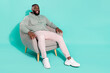 © deagreez - Full length body size view of attractive cheery guy sitting in armchair copy space isolated over bright teal turquoise color background