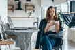 © undrey - A woman works at home, sitting at a table with a laptop and holding a mug