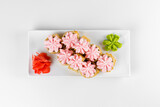 Fototapeta Maki - Japanese tempura hot sushi roll on white plate and background. Sushi pieces with salmon, eel, cucumber, cream cheese, avocado wrapped in rice with crunchy seaweed on top with greens