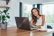 © undrey - Woman is sitting at the kitchen table with laptop