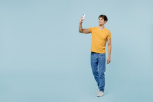 Full Body Young Man 20s In Yellow T-shirt Doing Selfie Shot On Mobile Cell Phone Post Photo On Social Network Isolated On Plain Pastel Light Blue Background Studio Portrait. People Lifestyle Concept