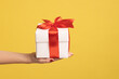 © khosrork - Closeup side view of woman hand holding out white gift box with red ribbon, giving present on holiday, bonuses and surprises concept. Indoor studio shot isolated on yellow background.