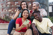 © EFStock - Latin and African American friends sharing social media content on smart phone. Diverse young people having fun using internet in a modern city (Barcelona)